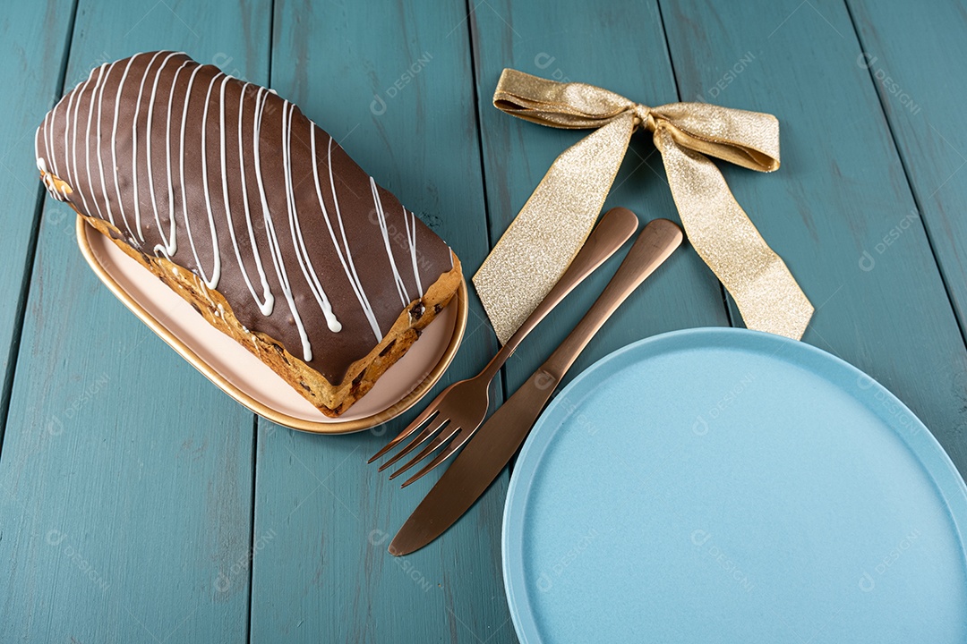 Chocotone com cobertura de chocolate ao lado de talheres, laço de fita