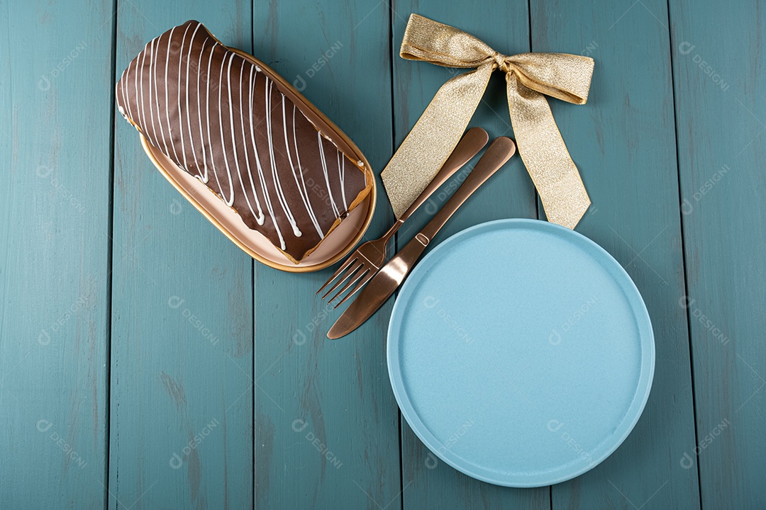 Chocotone com cobertura de chocolate ao lado de talheres, laço de fita