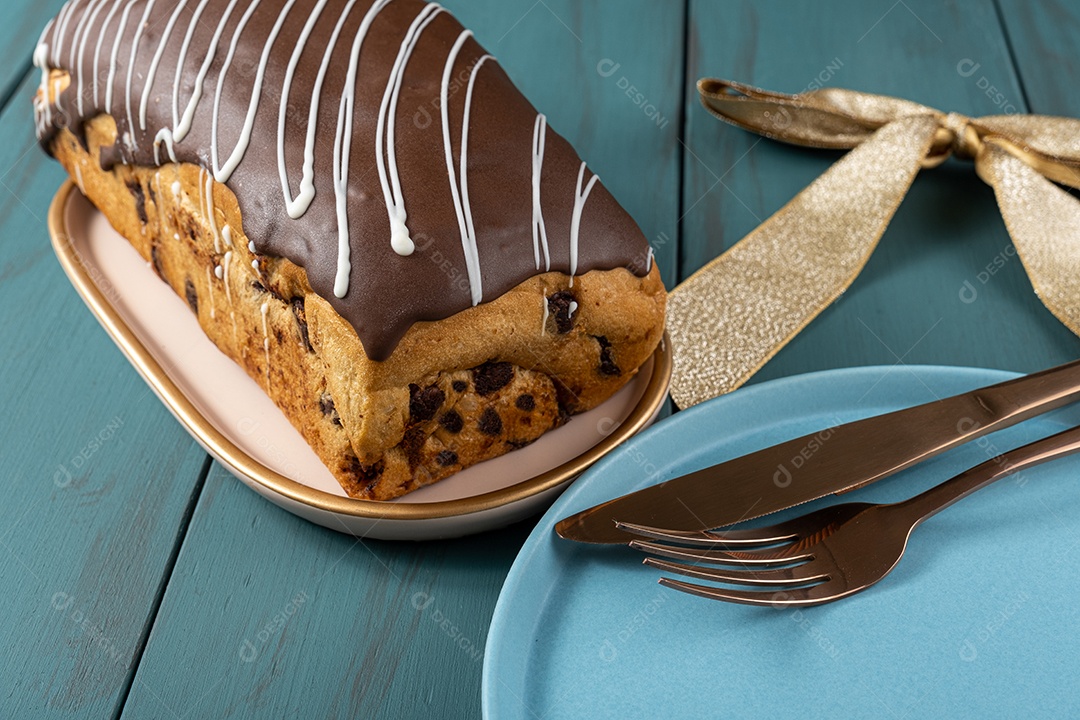 Chocotone com cobertura de chocolate ao lado de talheres, laço de fita