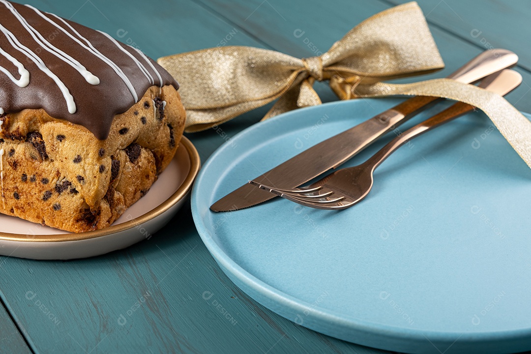 Chocotone com cobertura de chocolate ao lado de talheres, laço de fita