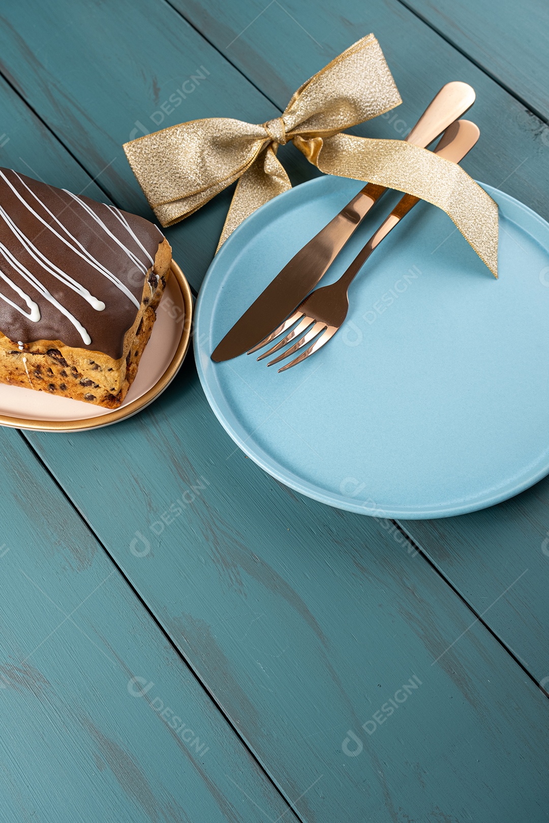 Chocotone com cobertura de chocolate e brilhos de vela, junto a talheres, laço de fita e prato