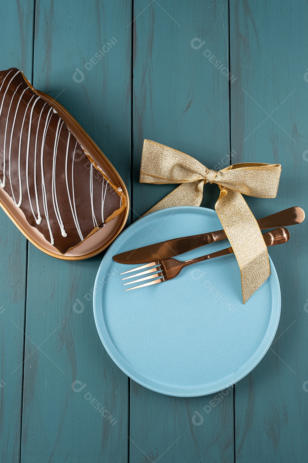 Chocotone com cobertura de chocolate e brilhos de vela, junto a talheres, laço de fita e prato