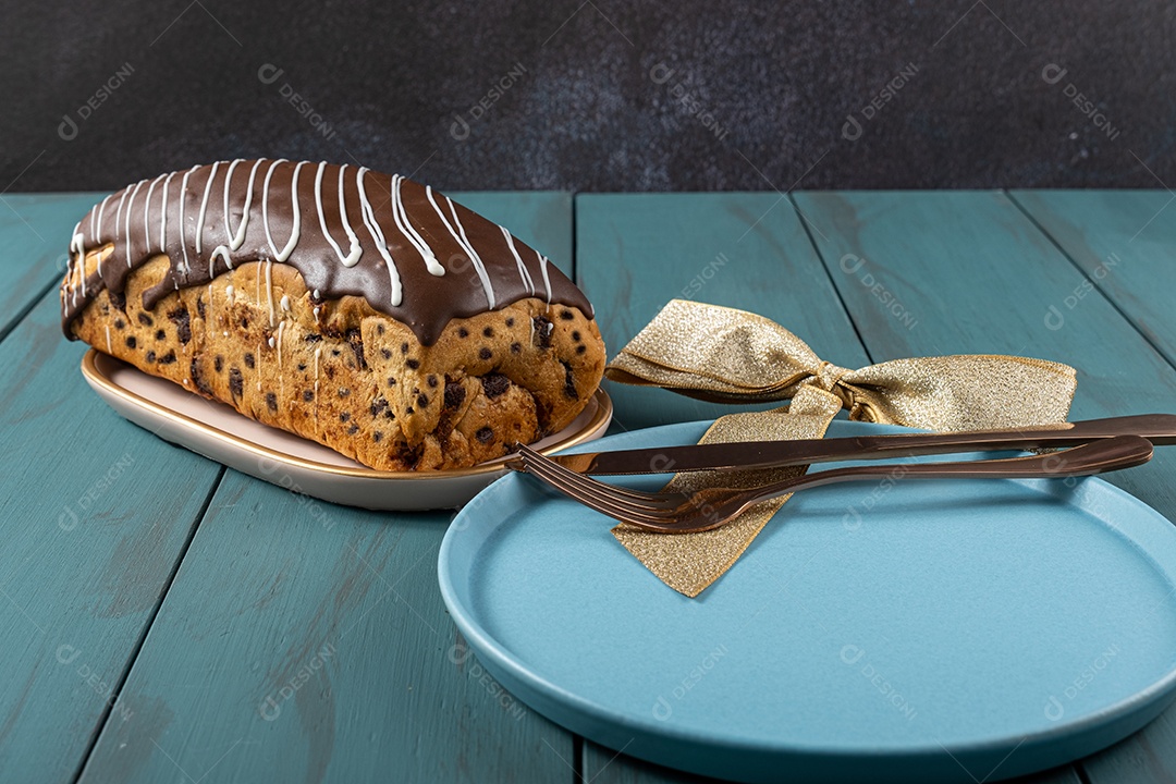 Chocotone com cobertura de chocolate e brilhos de vela, junto a talheres, laço de fita e prato