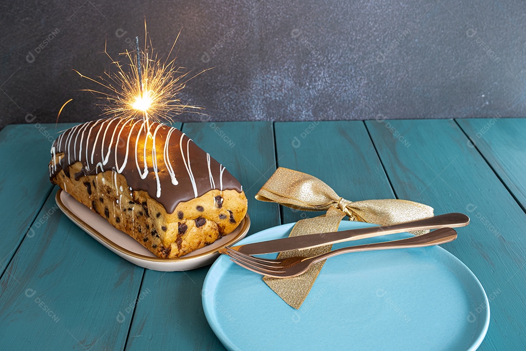 Chocotone com cobertura de chocolate e brilhos de vela, junto a talheres, laço de fita e prato