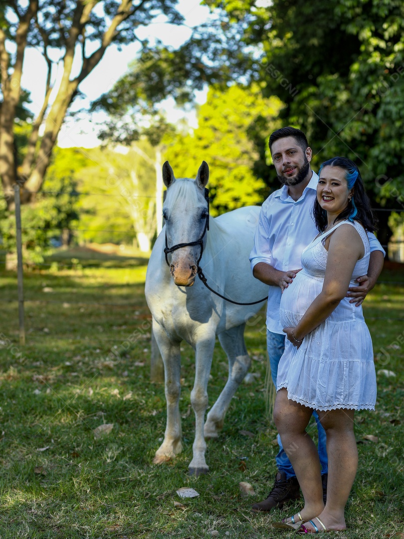 Homem com ao lado de sua esposa gravida ao lado de cavalo sobre uma fazenda