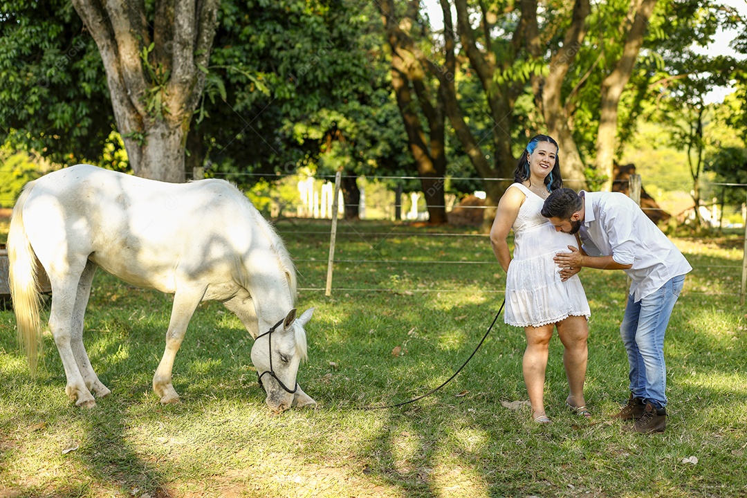 Homem com ao lado de sua esposa gravida ao lado de cavalo sobre uma fazenda