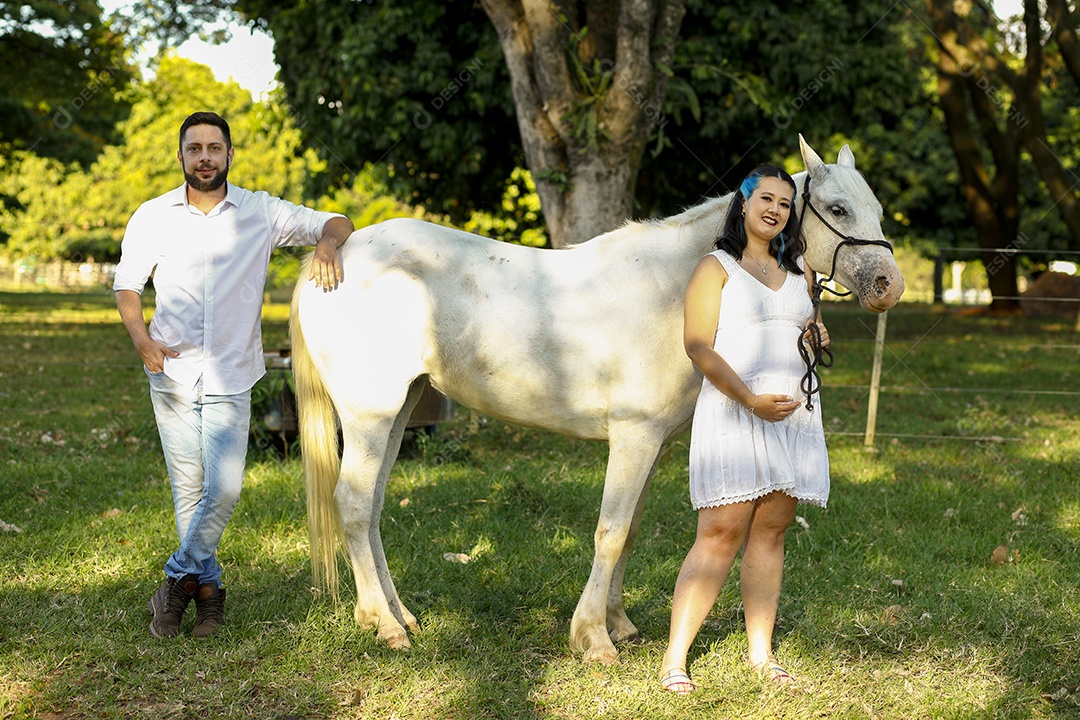 Homem com ao lado de sua esposa gravida ao lado de cavalo sobre uma fazenda