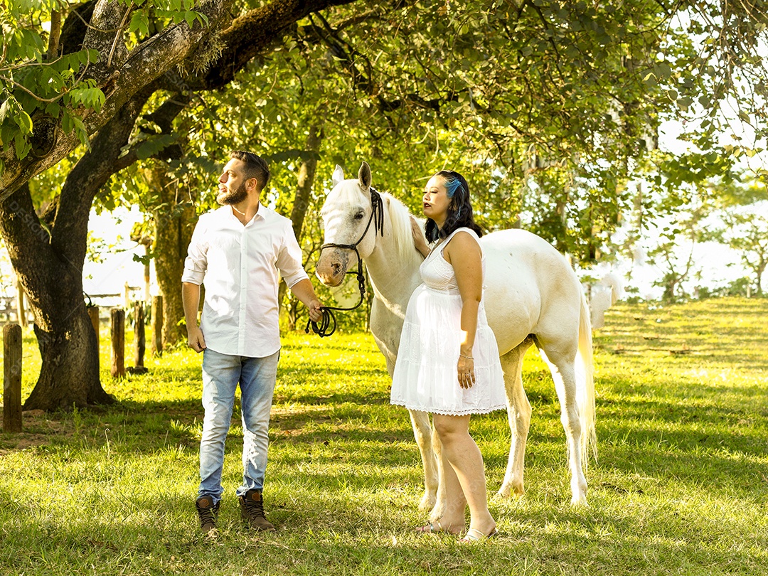 Homem com ao lado de sua esposa gravida ao lado de cavalo sobre uma fazenda