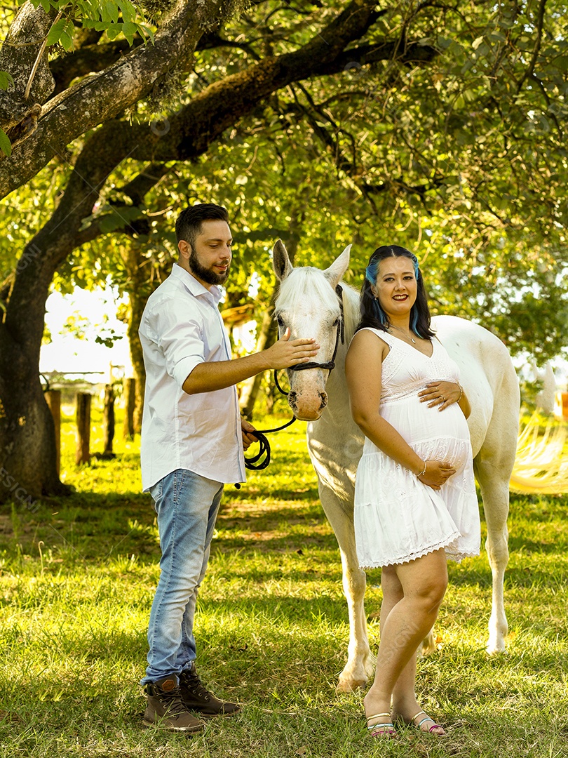 Homem com ao lado de sua esposa gravida ao lado de cavalo sobre uma fazenda
