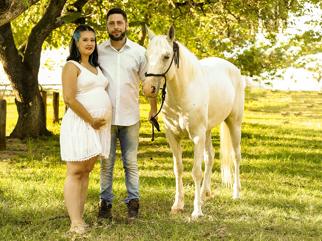 Homem com ao lado de sua esposa gravida ao lado de cavalo sobre uma fazenda