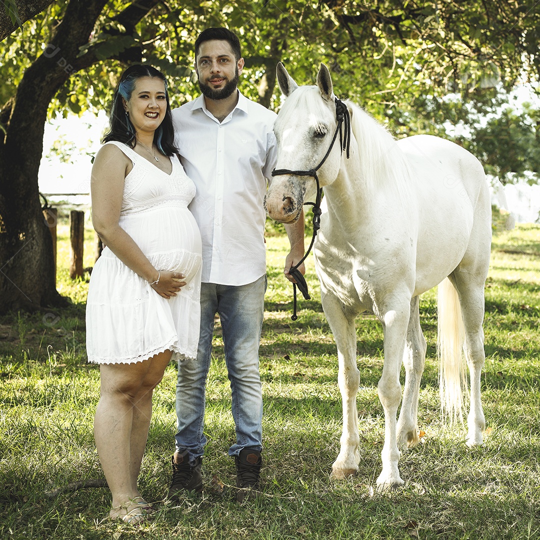 Homem com ao lado de sua esposa gravida ao lado de cavalo sobre uma fazenda