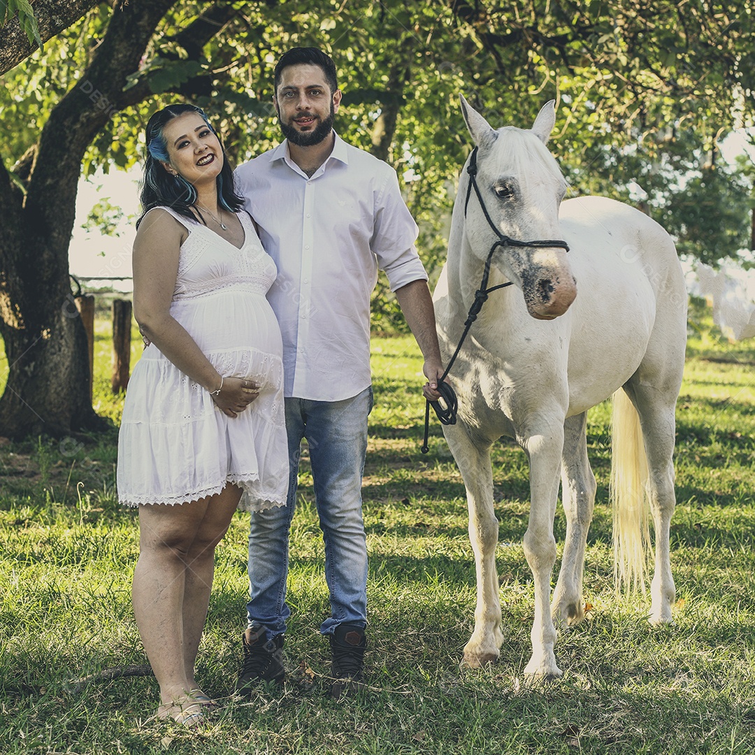 Homem com ao lado de sua esposa gravida ao lado de cavalo sobre uma fazenda
