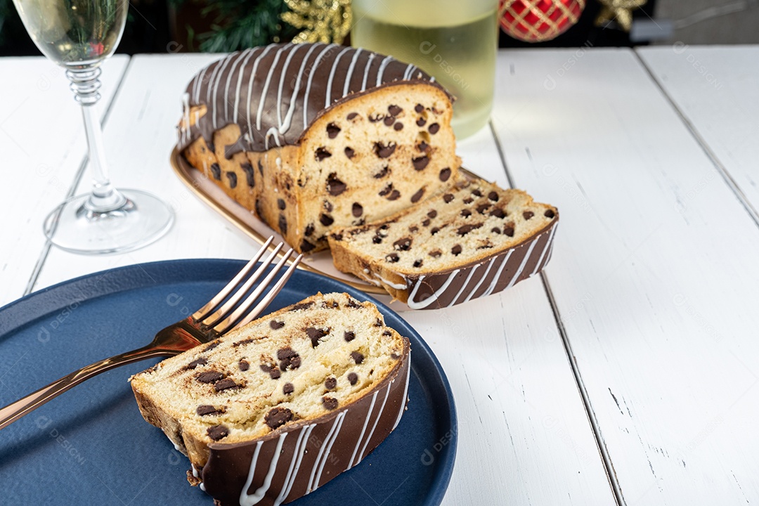 Detalhe da fatia de Chocotone rodeada por garfo, copo e garrafa de espumante