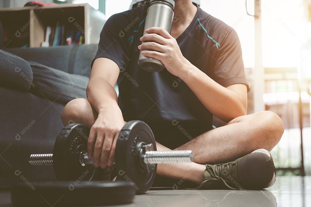 Homem bebendo proteína ou bebida de recuperação sentado no chão de uma academia após um treino