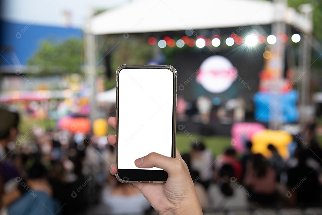 A mão segurando o smartphone móvel simula a tela branca em branco no festival de música no fundo do jardim