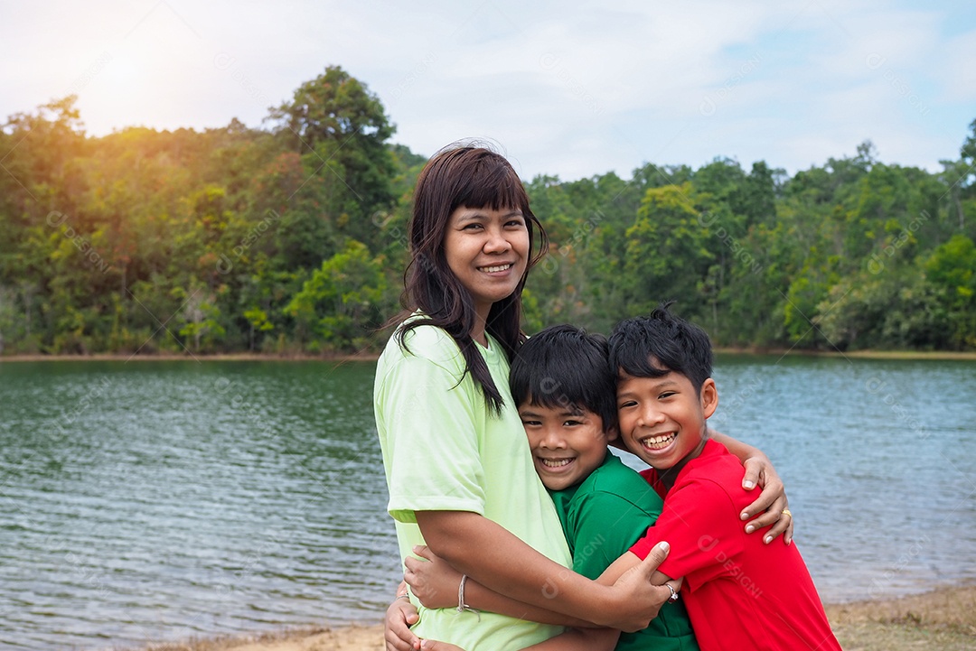 Família feliz passando tempo ao ar livre abraçando e apreciando a vista do rio. Mãe com dois filhos.