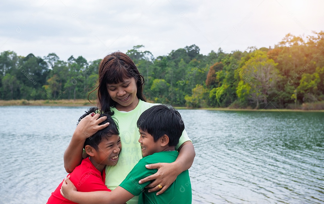 Família feliz passando tempo ao ar livre abraçando e apreciando a vista do rio. Mãe com dois filhos.