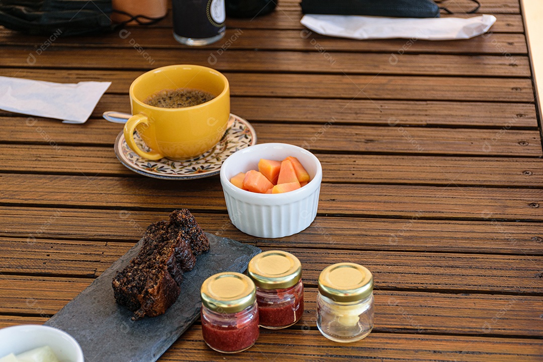 Bolo de biscoito ao lado de uma porção de mamão e geleias variadas.
