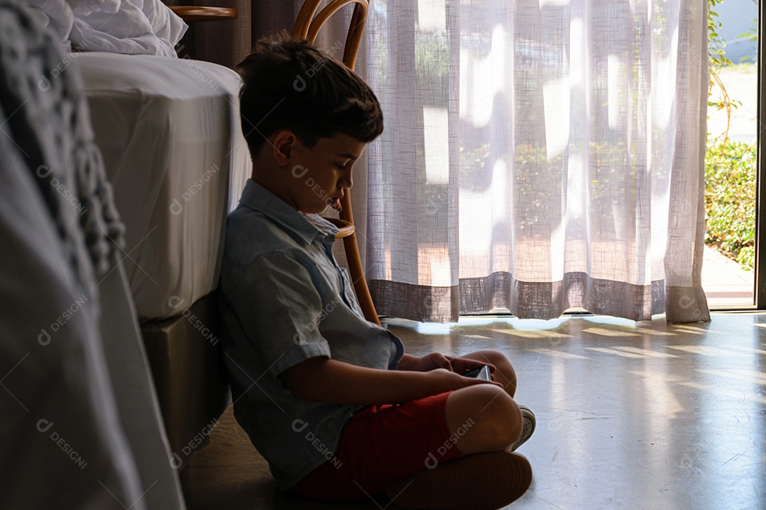 criança de 8 anos sentada no chão e brincando com seu smartphone.