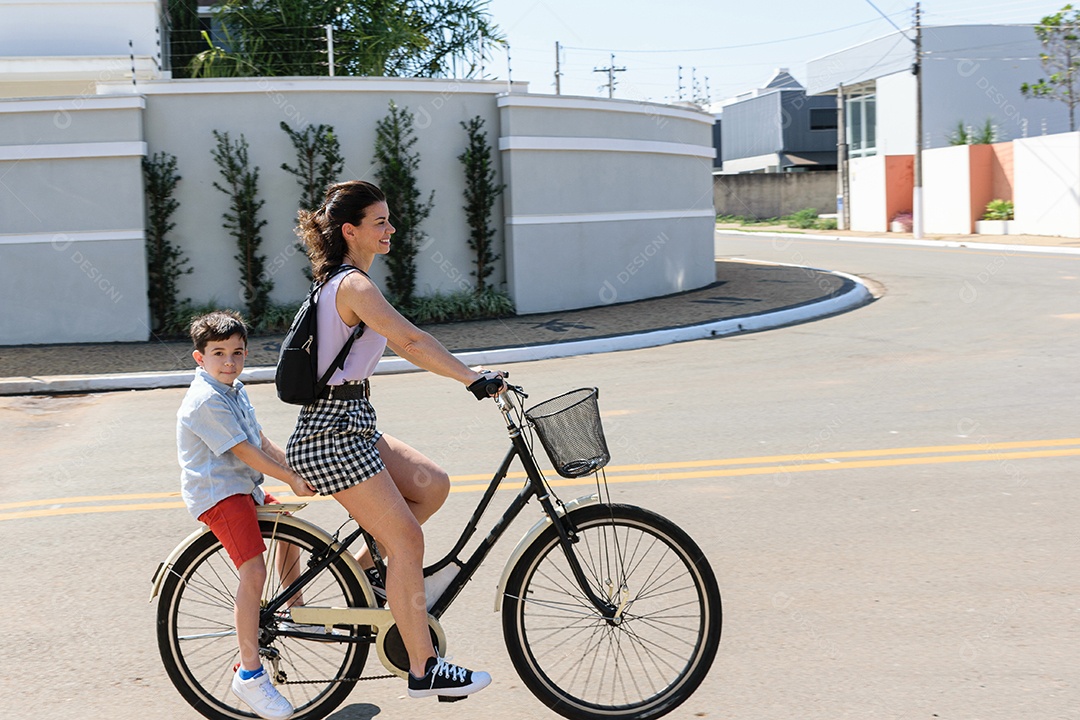 Mãe e filho brasileiros andando de bicicleta em uma manhã ensolarada.