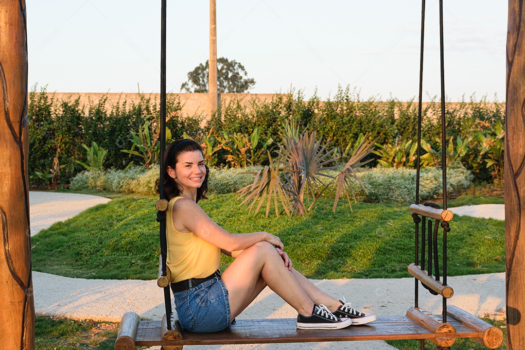 Mulher brasileira sentada em um balanço de madeira, sorrindo