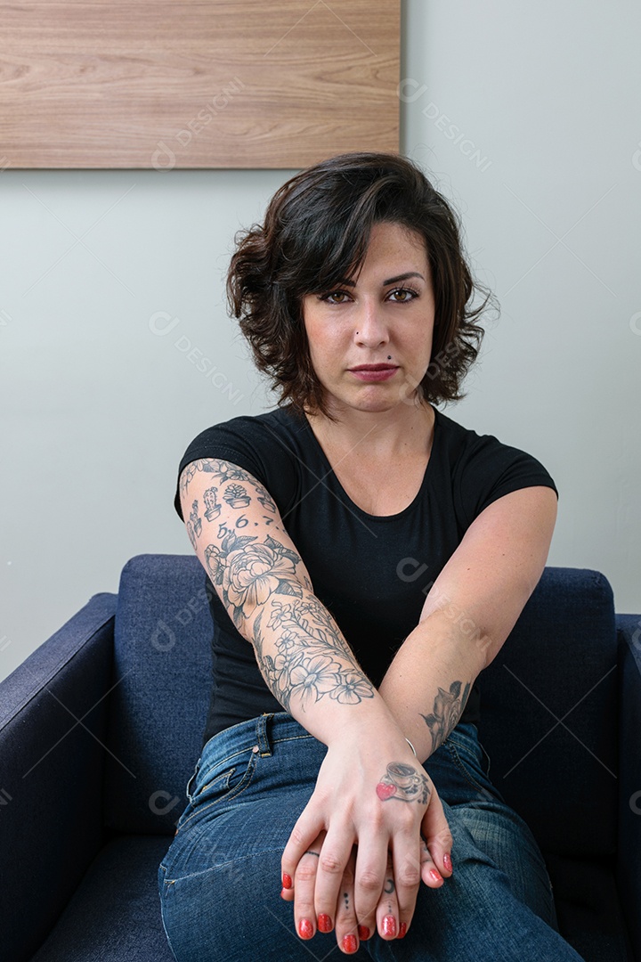 Mulher brasileira, tatuada, com as mãos cruzadas e de frente para a câmera