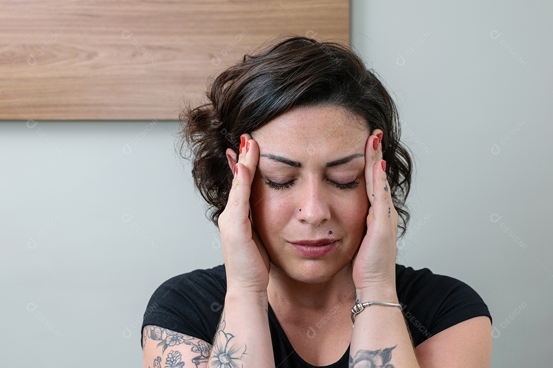 Close de brasileira, tatuada, com as mãos na têmpora e com dor de cabeça.