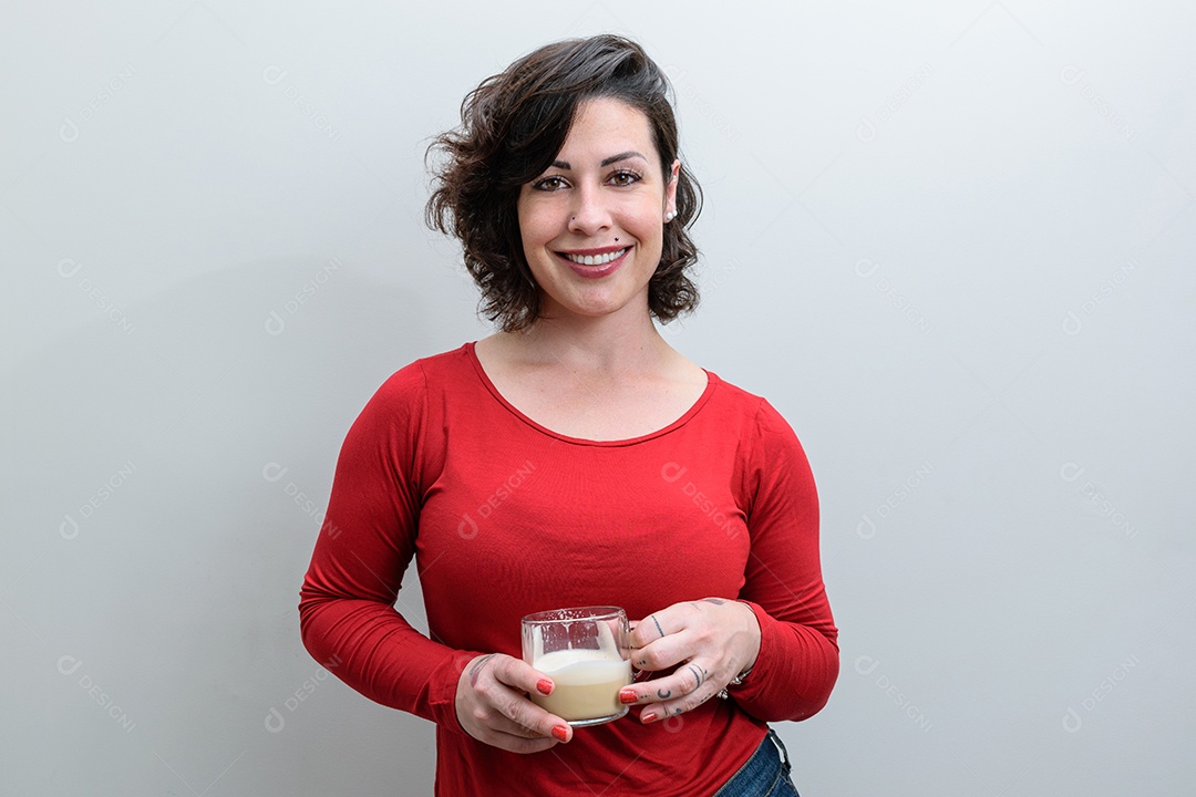 Mulher brasileira sorridente de frente para a câmera e segurando uma xícara de cappuccino
