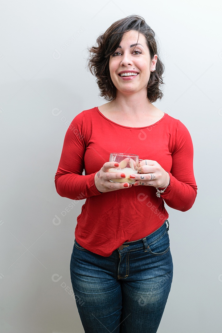 Mulher brasileira apertando os joelhos, sorrindo e segurando uma caneca de cappuccino