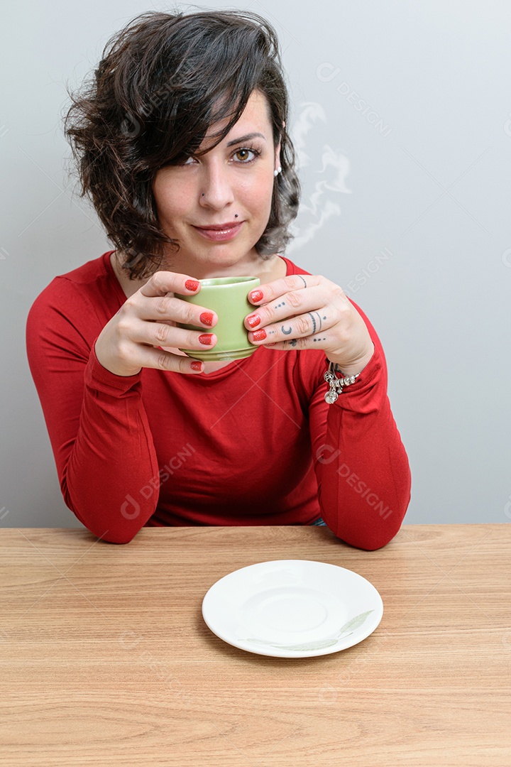Mulher brasileira, com o cabelo cobrindo um olho, com uma xícara de café
