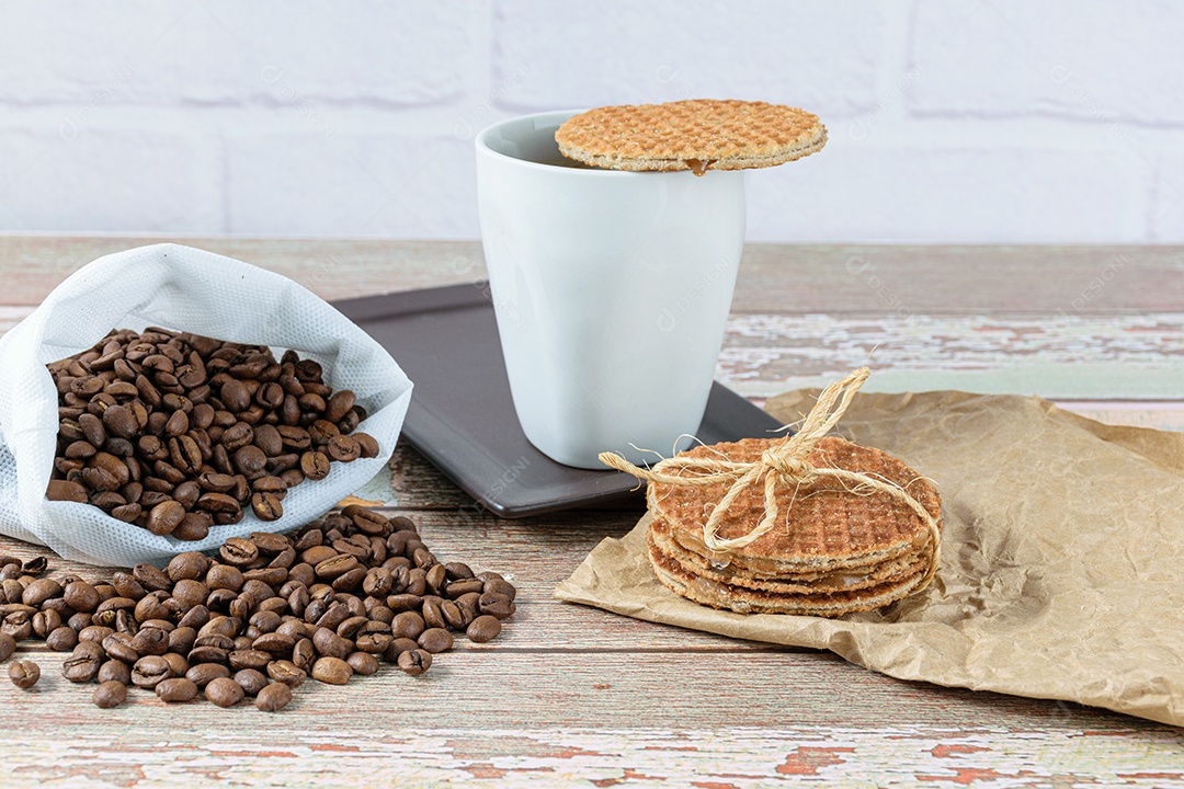 Biscoitos Stroopwafel com laço de sisal ao lado de uma xícara de café.
