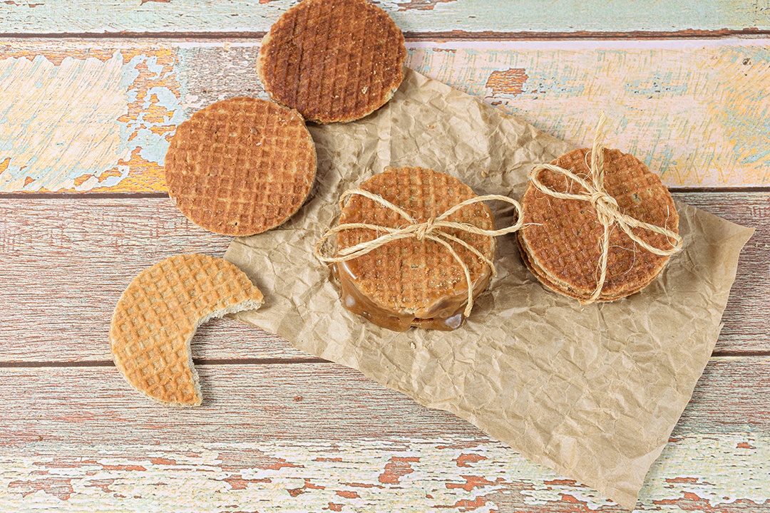 Empilhe stroopwafels em papel pardo, ao lado de outro biscoito com uma mordida.