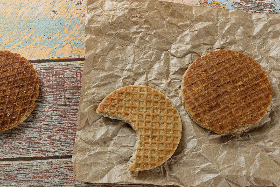 Stroopwafel com uma mordida em papel pardo ao lado de outro biscoito