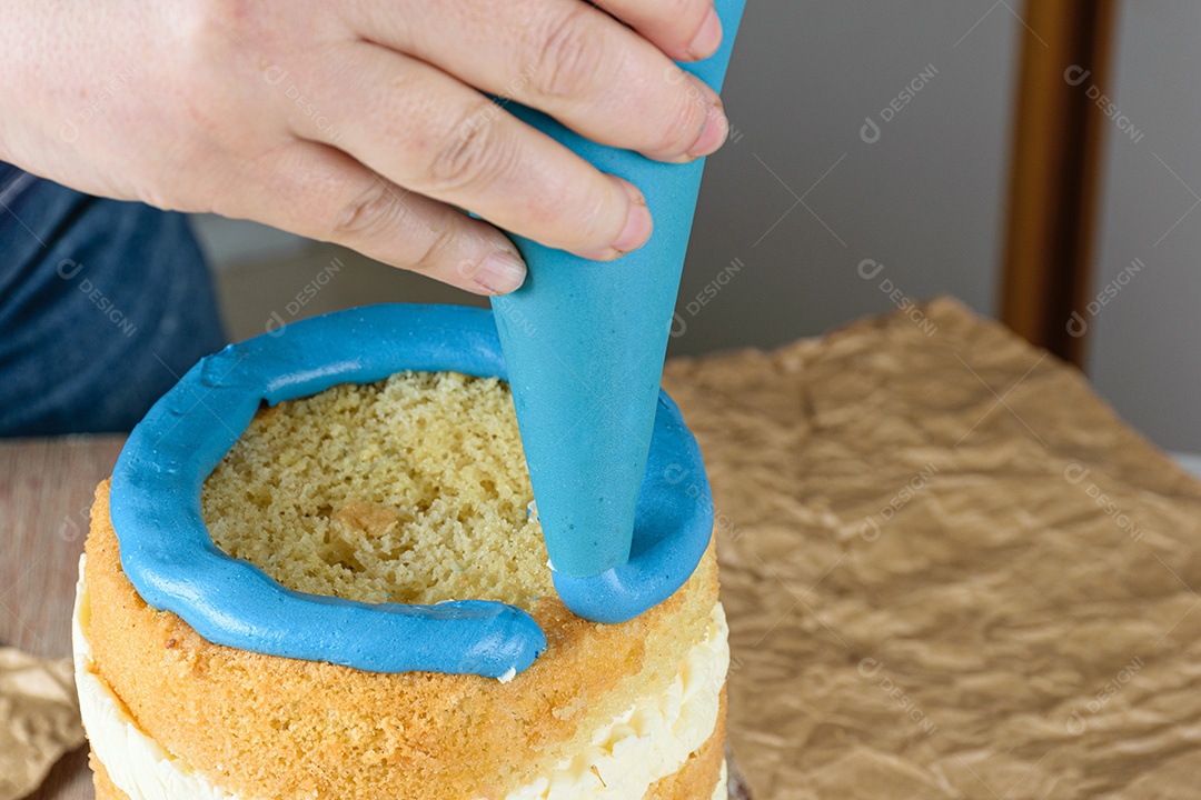 Baker usando um bico de confeiteiro para colocar glacê azul em cima do bolo.