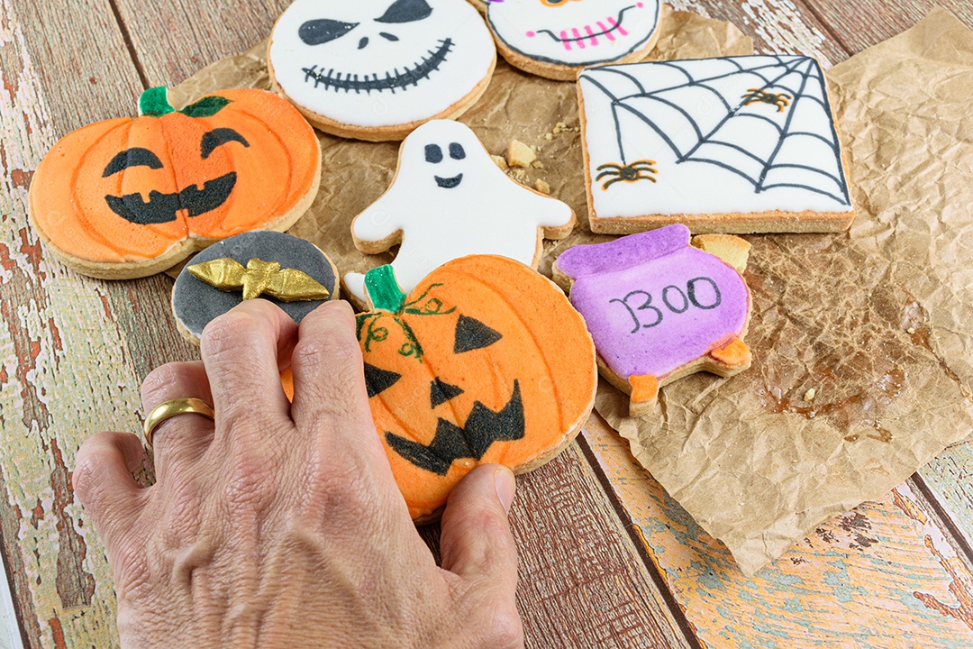 Mão masculina pegando um biscoito amanteigado em forma de abóbora