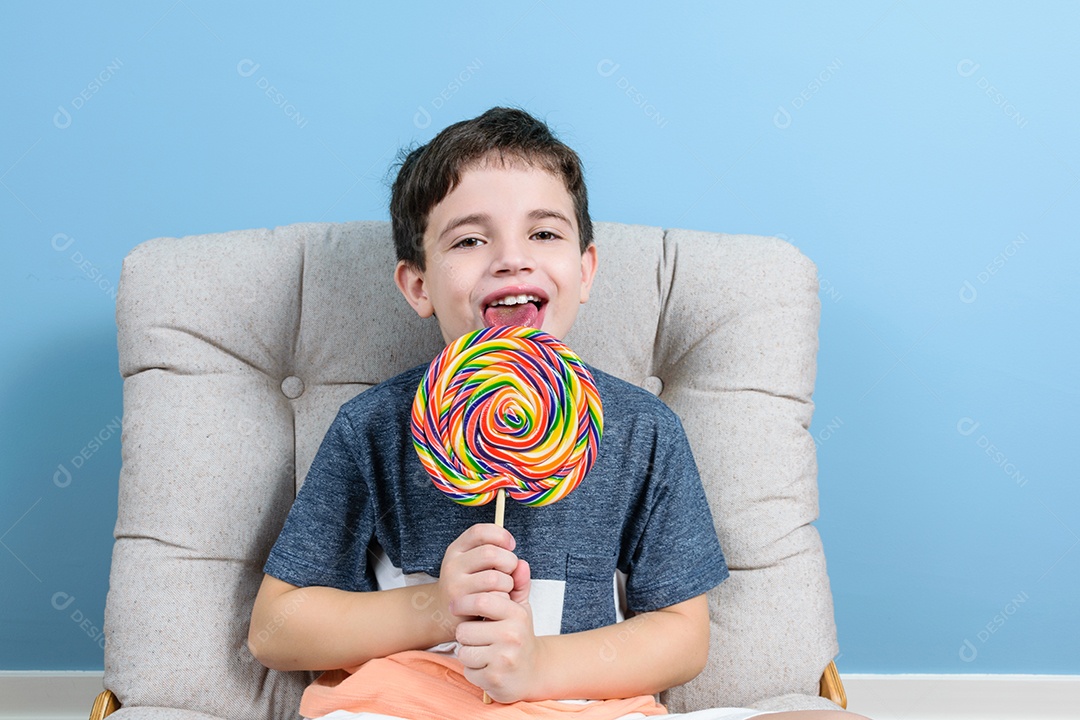 Brasileiro de 8 anos lambendo um grande pirulito e sentado na poltrona