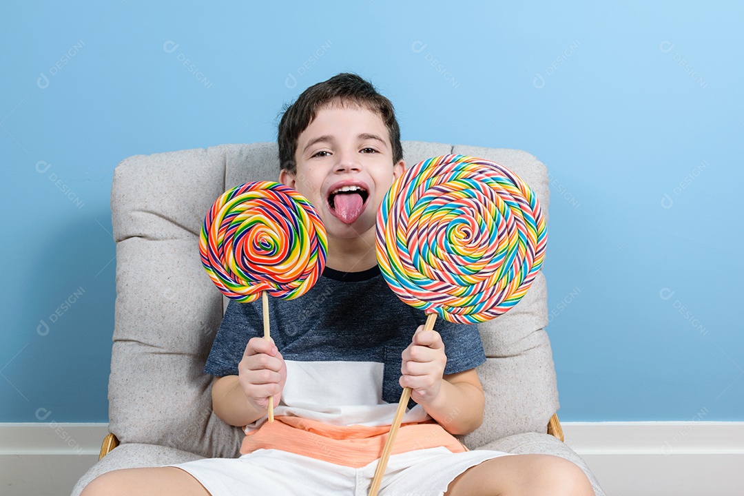 Brasileiro de 8 anos segurando dois pirulitos grandes e mostrando a língua