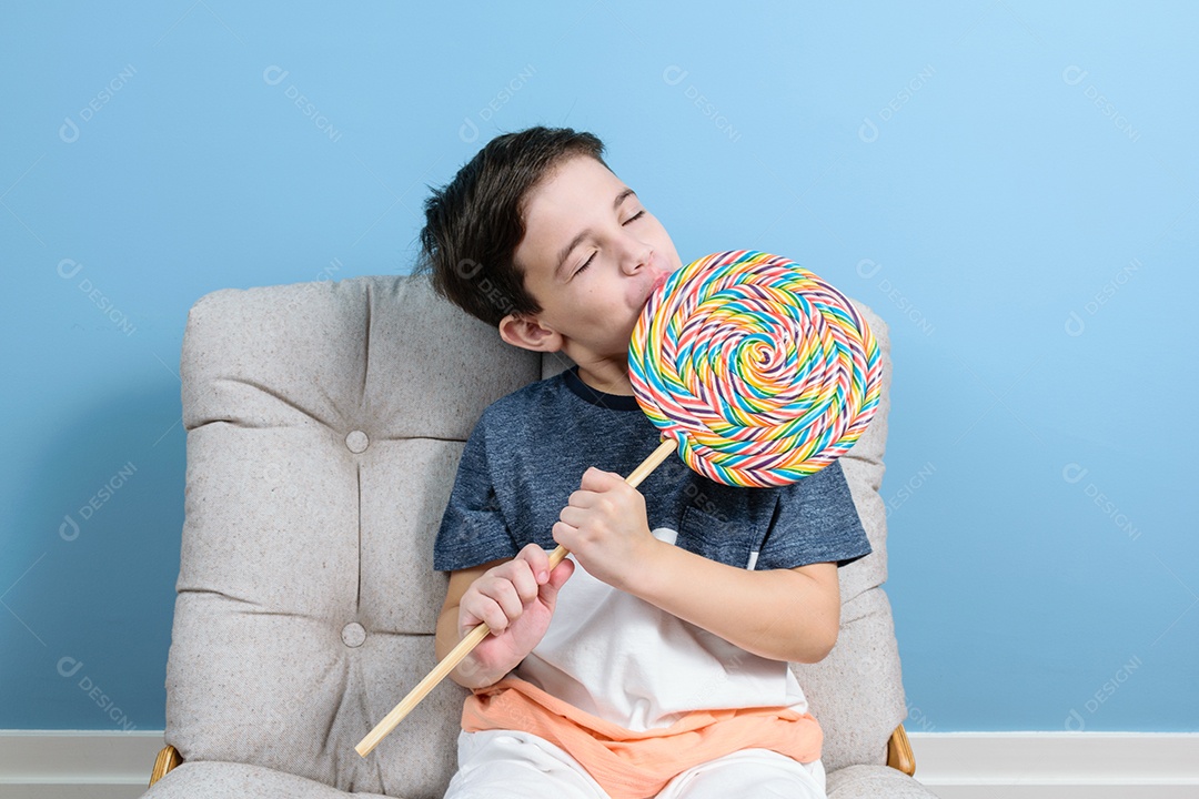 criança de 8 anos segurando e lambendo um grande pirulito colorido