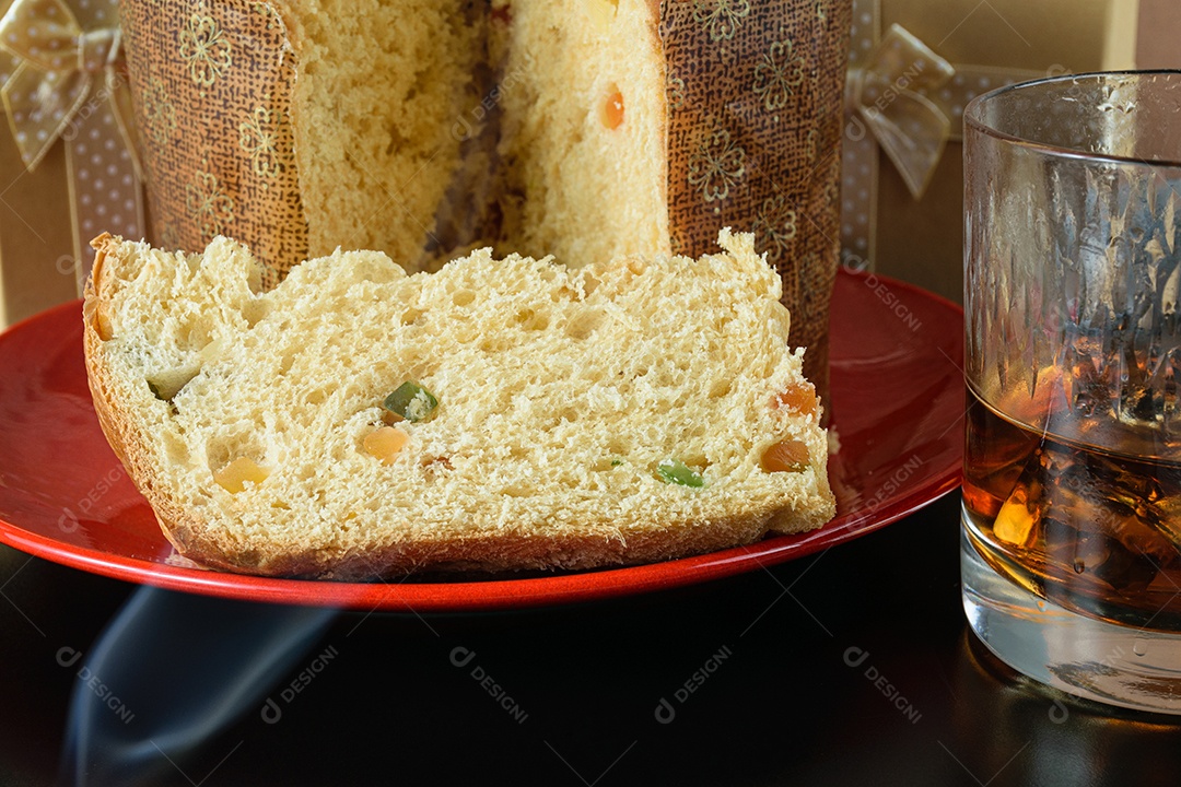 Close de uma fatia de panetone sob fumaça de cigarro, ao lado de um copo de uísque