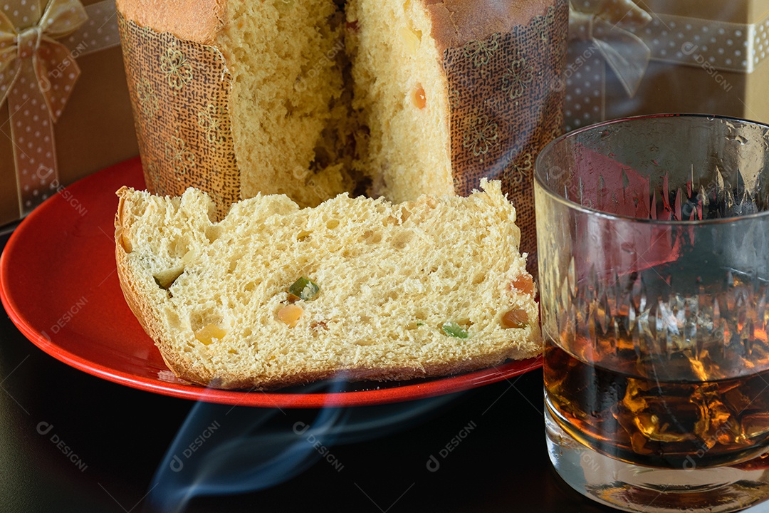 Close de uma fatia de panetone sob fumaça de cigarro, ao lado de um copo de uísque