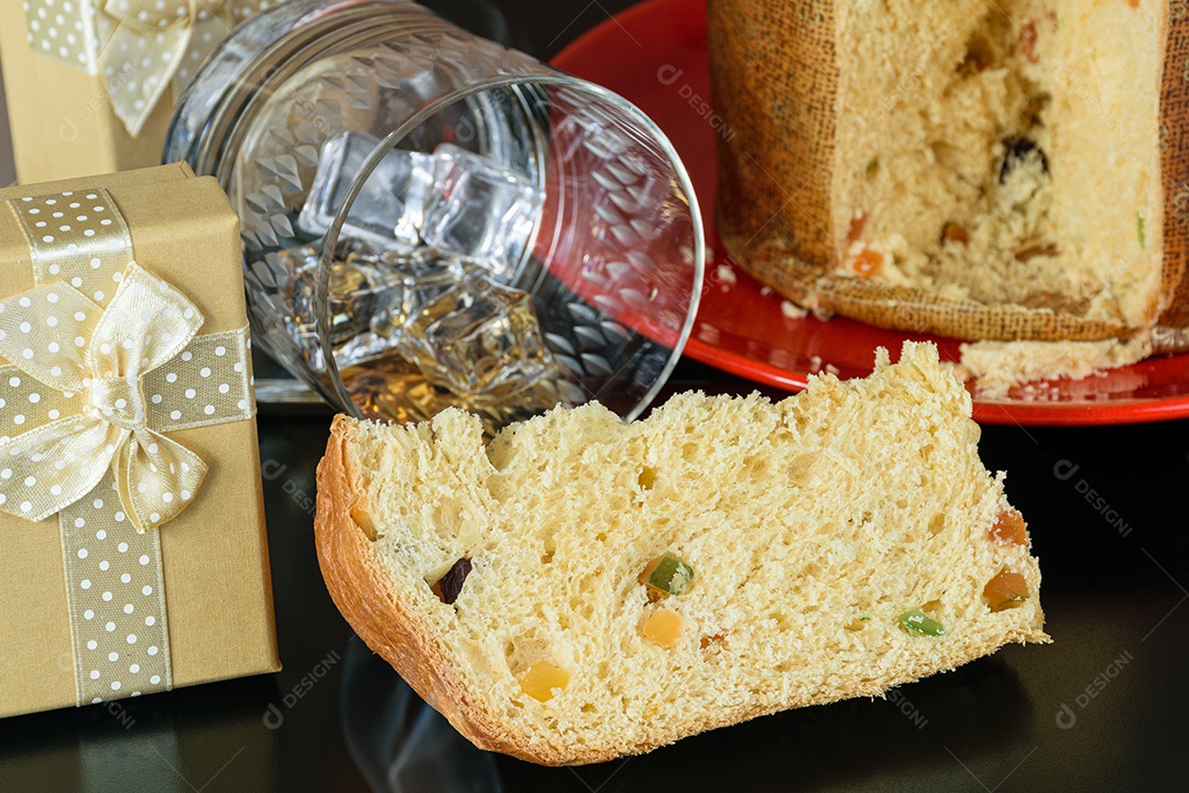 Fatia de panetone ao lado de uma caixa de presente e um copo virado