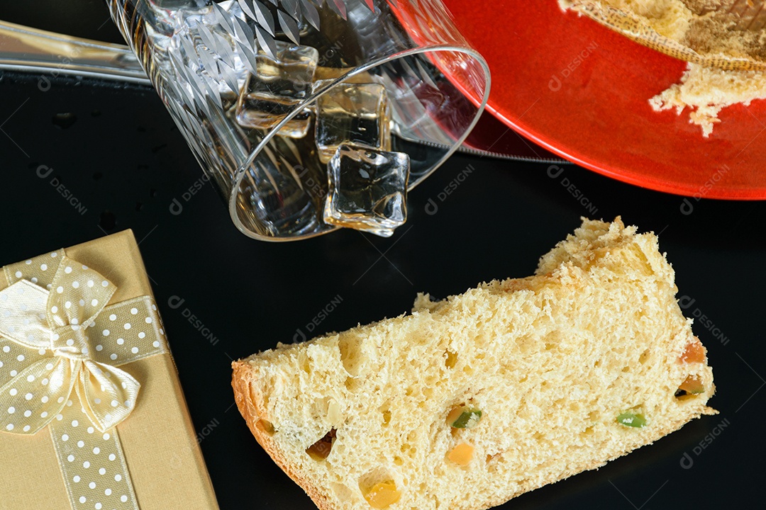 Fatia de panetone ao lado de uma caixa de presente e um copo virado
