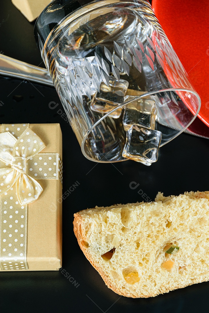Fatia de panetone sob fumaça de cigarro, ao lado de caixa de presente e copo de uísque virado