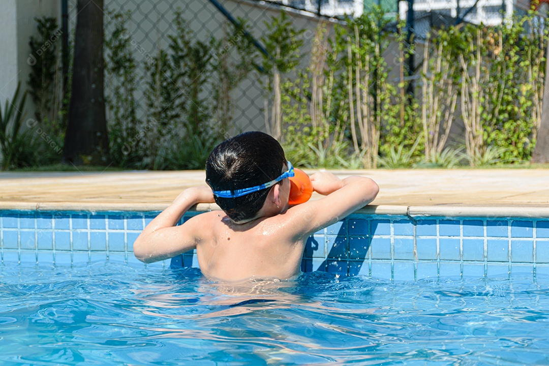 Criança de 8 anos encostada na beira da piscina e segurando