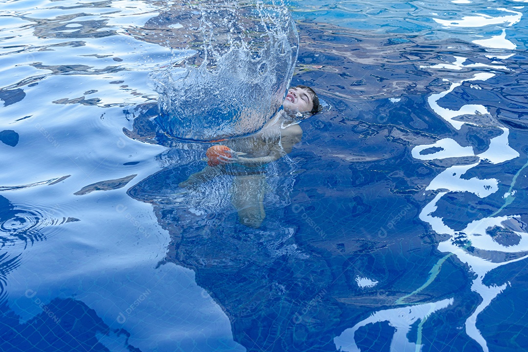 Menino de 8 anos na piscina sendo coberto por uma coluna de água de uma bomba dágua