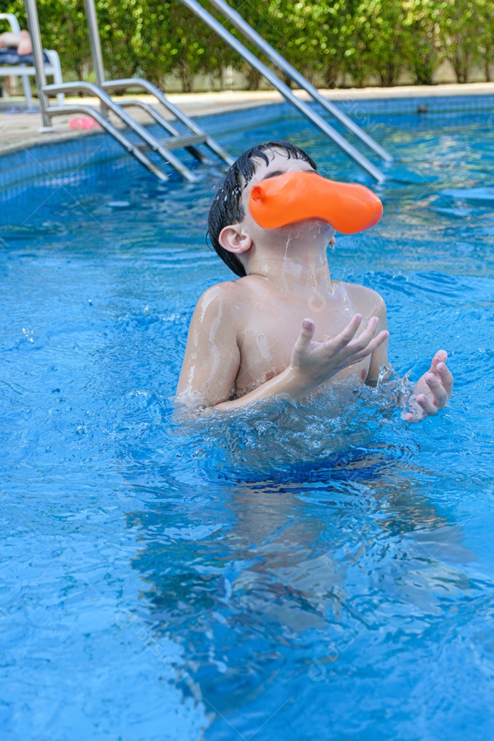 Menino de 8 anos na piscina sendo atingido no rosto por uma bomba de água.