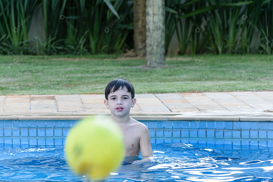 Criança de 8 anos na piscina olhando a bola que foi lançada