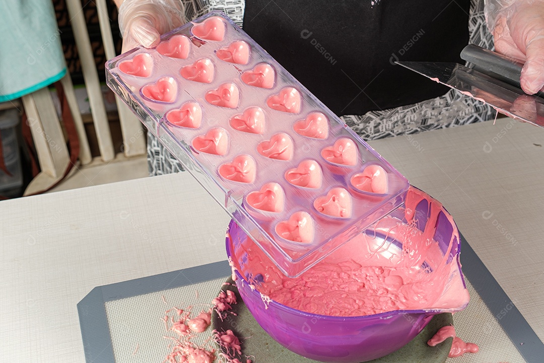 Confeiteiro com espátula para retirar o excesso de ganache de morango em uma forma de policarbonato