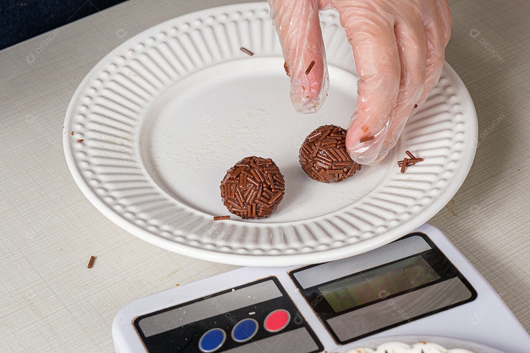 Detalhe de brigadeiros com granulado de chocolate sendo pesados