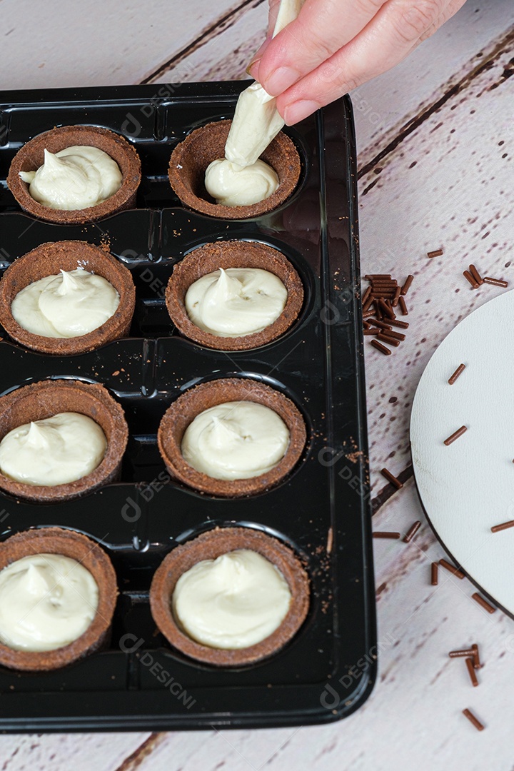 Foco seletivo. Detalhe do bocal de confeiteiro enchendo mini tortas